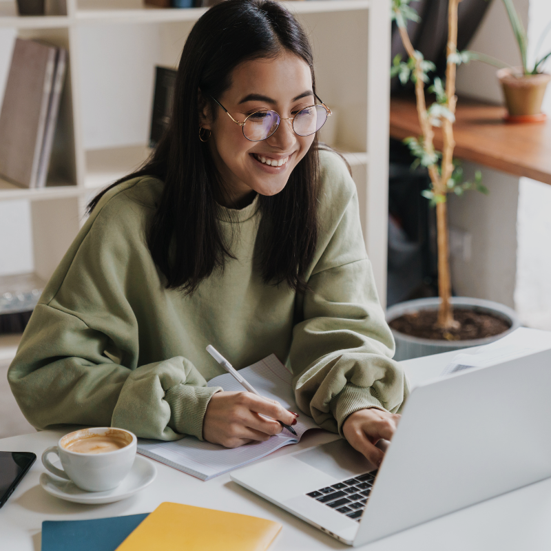Woman working on a laptop at a desk with a cup of coffee and notebook.